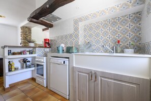 A kitchen with a stone wall, a coffee maker, a dishwasher, and a tiled backsplash. - Country House "Maison Bourgues" with Cliff View, Wi-Fi, and Air Conditioning (Lioux)