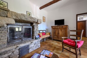 Un salon avec une cheminée en pierre, un meuble en bois, un téléviseur et un fauteuil avec un coussin rouge.