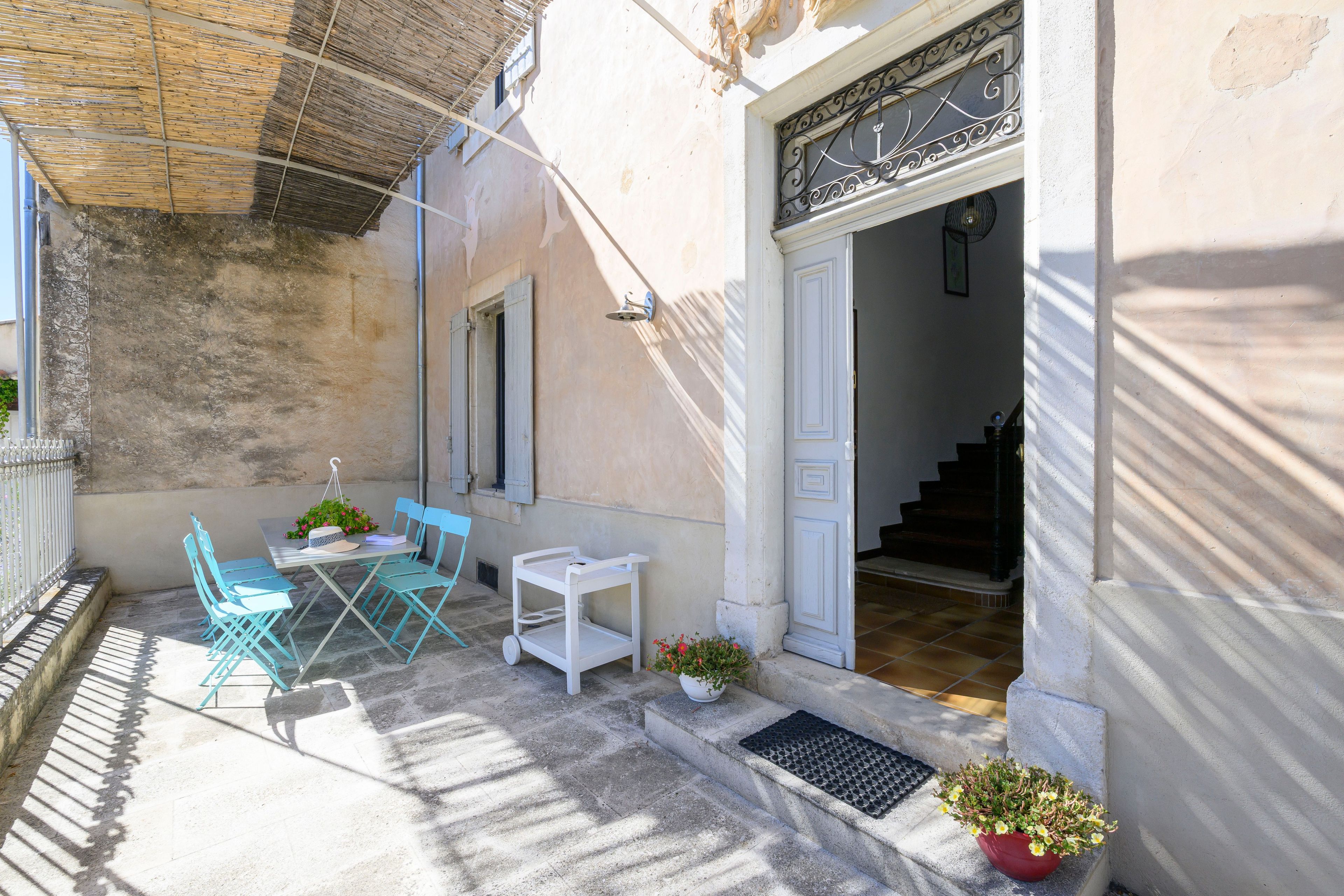 A courtyard with a table and chairs, a hanging plant, and a staircase leading to an upper floor.