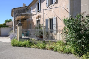 Ein Haus mit überdachter Veranda, einem Metallzaun und einem Garten mit verschiedenen Pflanzen.