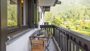 Un balcón con mesa y sillas, con vistas a un valle boscoso.