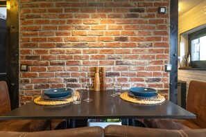 Un coin repas avec un mur en briques, deux assiettes bleues, deux verres à vin et un ensemble de salière et de poivrière en bois.