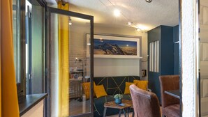 Una sala de estar moderna con un sofá, una mesa de centro y una silla. Hay una puerta de vidrio que da a otra habitación.