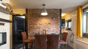 Una cocina con pared de ladrillo, una mesa de comedor con sillas, una lámpara colgante y una ventana con cortinas amarillas.