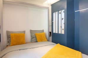 Une chambre à coucher avec un lit, deux oreillers, une porte bleue et un mur blanc.