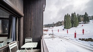 Ein Holzhaus mit Balkon, zwei weißen Metallstühlen und einem Tisch.