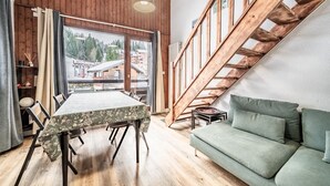 Ein Zimmer mit Esstisch, einer Couch, einer Holztreppe und einem großen Fenster mit Blick auf Gebäude und Bäume.