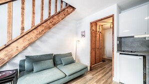 Ein modernes Wohnzimmer mit einer Holztreppe, einer Couch, einem Kühlschrank und einem Flur, der zu einer Holztür führt.