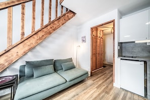 Een moderne woonruimte met een houten trap, een bank, een koelkast en een gang naar een houten deur.