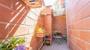 A narrow outdoor patio with brick walls, wooden planters with plants, and a small table with chairs. - Mostaza Ilofts (Medellín)