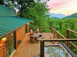 Une cabane en bois dotée d’une terrasse, d’un bain à remous et offrant une vue sur une chaîne de montagnes boisées.