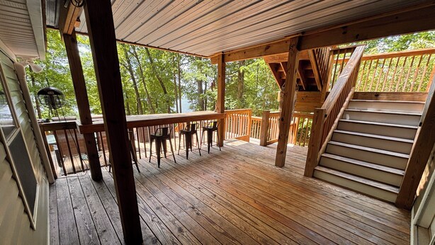 Une terrasse en bois avec un escalier menant à un niveau supérieur, le tout entouré d’arbres.