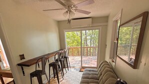 Un vaste espace de vie doté d’un plancher en bois, d’un canapé, d’une table à manger avec des chaises, d’un ventilateur de plafond et d’une porte-fenêtre coulissante donnant sur une terrasse.