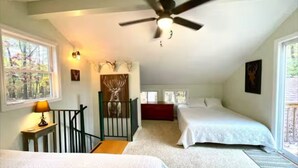Une chambre avec deux lits, un ventilateur de plafond, une fenêtre donnant sur les arbres et une petite table avec une lampe.