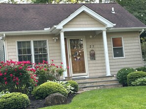 A single-story house with a beige exterior, a dark roof, and a front door with a number '27' displayed. - Walk to beach in this charming home with ac and wifi (Riverhead)