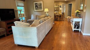 A living room with a sofa, a TV, a dining area with chairs and a table, and a hallway leading to another room.