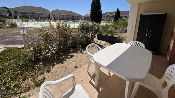 A patio with a table and chairs, overlooking a swimming pool and residential buildings. - 226 - Comfortable apartment in a residence with swimming pool in Verdon sur Mer (LE VERDON SUR MER)