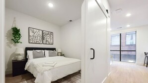 A modern bedroom with a large bed, a hanging plant, and abstract wall art. - Cozy 1BR/1BA + Gym Near UPMC & Carnegie Mellon (Pittsburgh)