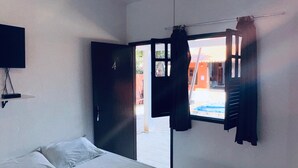 Ein Schlafzimmer mit Bett, Deckenventilator, Fenster mit Vorhängen und Blick ins Freie.