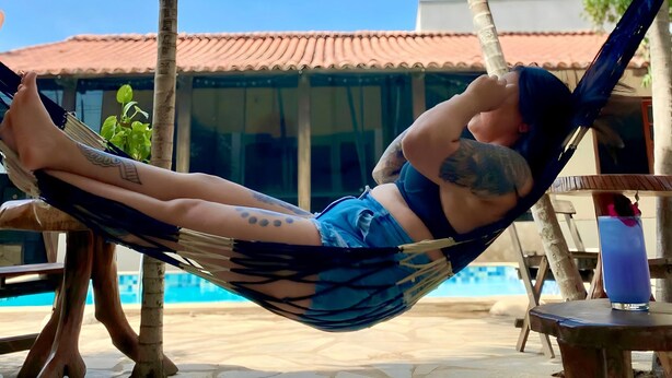 Eine Person entspannt in einer Hängematte am Pool mit einer gefliesten Terrasse und Palmen.
