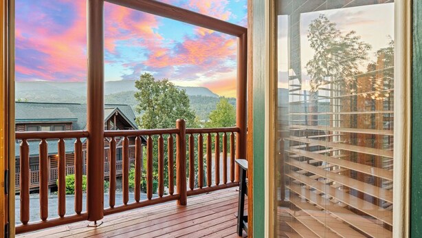A wooden deck with a view of mountains and a colorful sky.