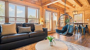 A cozy cabin interior with a black leather sofa, a hanging chair, and a dining area with a table and chairs.
