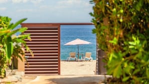 Eine Sitzgelegenheit am Strand mit zwei Stühlen und einem Tisch unter einem rosa Sonnenschirm mit Blick aufs Meer.