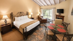 Habitación de hotel con cama, lámparas de noche, sofá, mesa de comedor con sillas, televisor y chimenea.