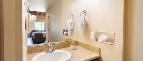 A bathroom with a granite countertop, a white sink, a mirror with lights, and a small potted plant.