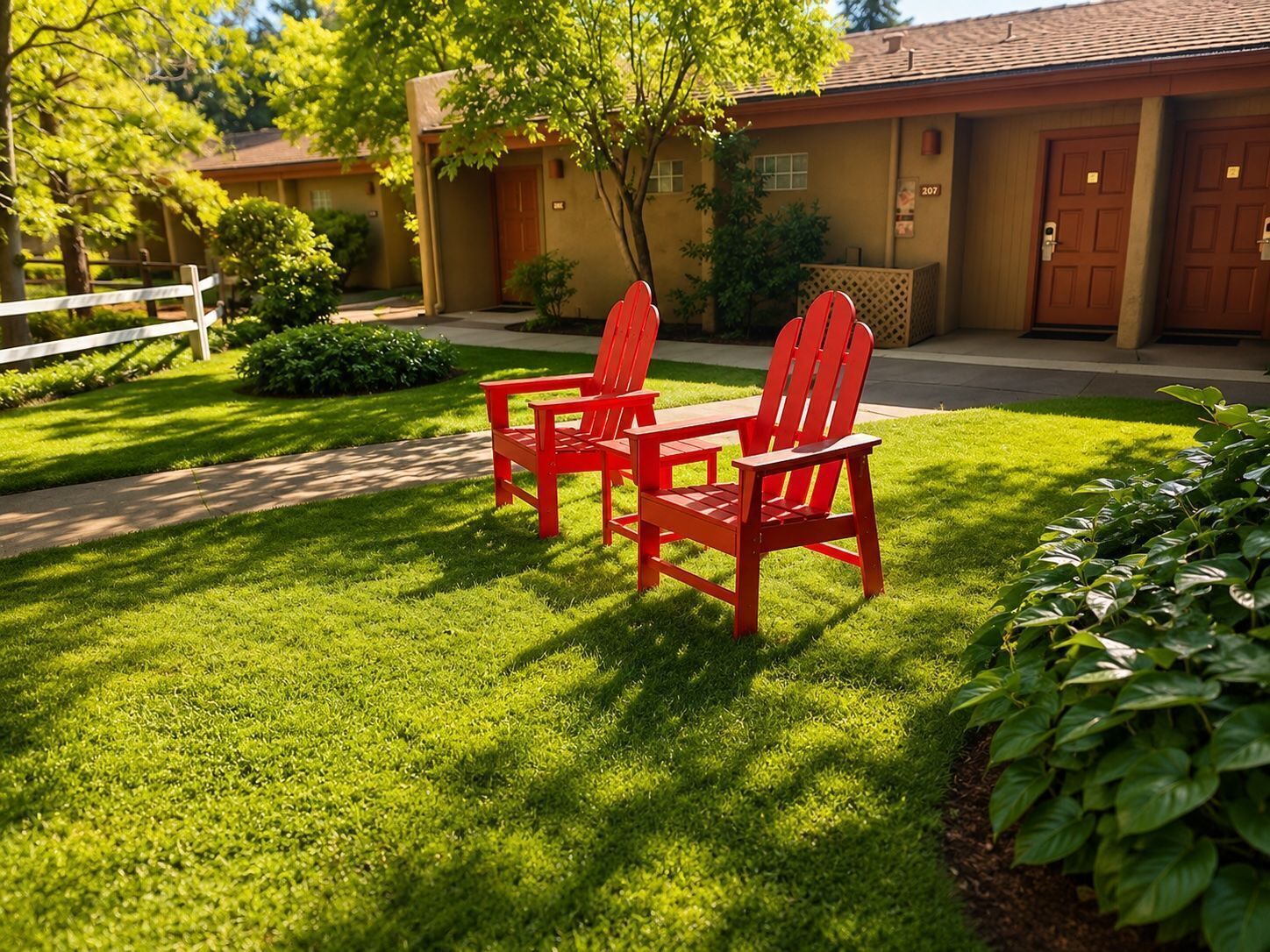 A well-maintained lawn with two red Adirondack chairs and a wooden bench.
