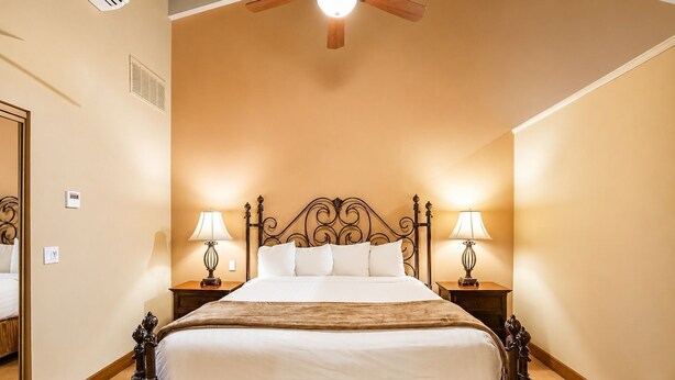 Een hotelkamer met een groot bed, twee nachtkastjes met lampen, een plafondventilator en een spiegel aan de linker muur.