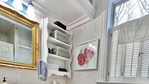 A bathroom with a white vanity, a toilet, a shelf unit, and a window with shutters. - CHARMING APARTMENT WITH SEPARATE ENTRANCE (southampton)