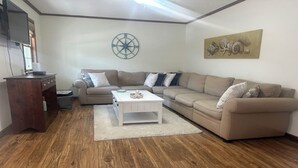 A living room with a wooden floor, beige sofas, a white coffee table, a wooden cabinet, a television, and a compass wall decoration. - Charming 2-bedroom condo with WiFi, AC in fantastic North Ocean City (Ocean City)