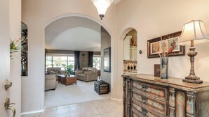 Ein geräumiges Wohnzimmer mit Kamin, Ledersofas und einem Couchtisch. Es gibt ein Holzschränkchen mit einer Lampe und einem gerahmten Bild an der Wand.