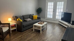 Un salon avec un canapé gris, une table basse, un meuble pour la télévision et une plante.