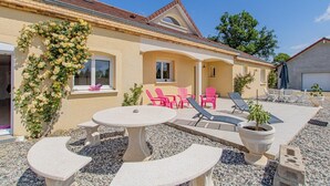 A house with a patio area featuring a round table, pink chairs, and lounge chairs. - Les Portes Roses - VARENNE SAINT GERMAIN (VARENNE SAINT GERMAIN)