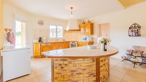 A kitchen with a central island, wooden cabinets, a microwave, and a sink. - Les Portes Roses - VARENNE SAINT GERMAIN (VARENNE SAINT GERMAIN)