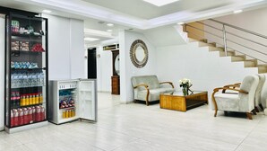 A modern living room with a built-in refrigerator stocked with beverages, a coffee table, two armchairs, and a staircase. - Hotel Tiwintza Internacional (Quito)