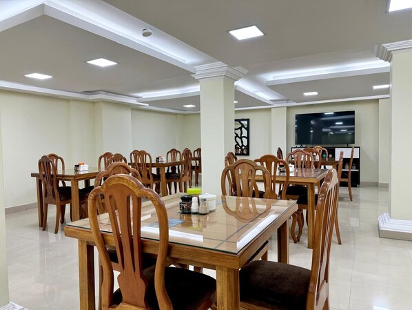 A spacious dining area with multiple wooden tables and chairs, a flat-screen TV mounted on the wall, and a modern ceiling design with recessed lighting. - Hotel Tiwintza Internacional (Quito)