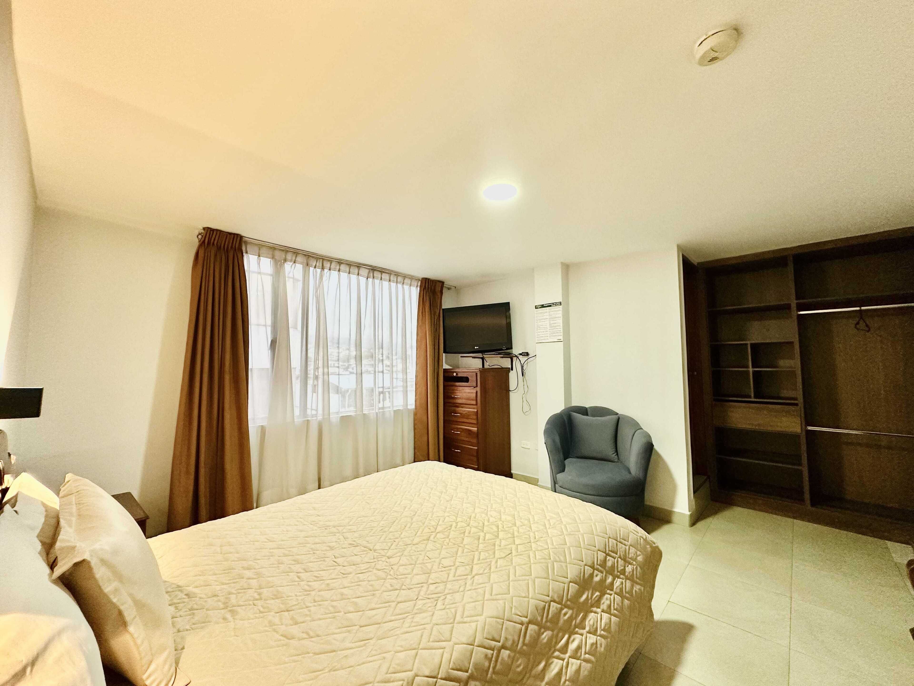 A hotel room with a bed, a chair, a TV, and a wardrobe.