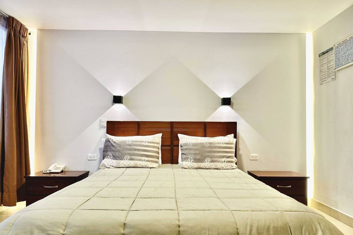 A hotel room with a large bed, two bedside tables, a telephone, and a wall-mounted light fixture.