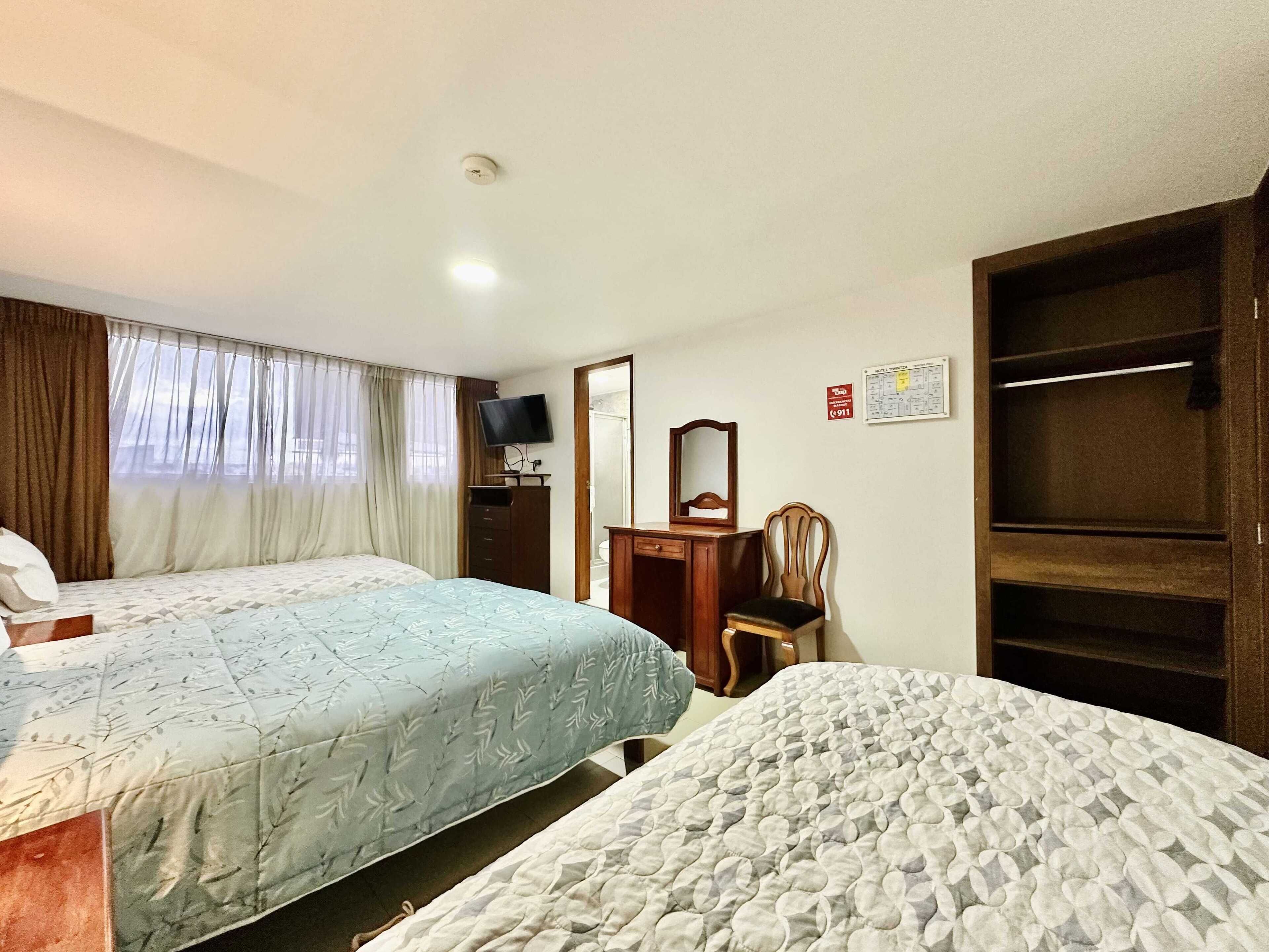 Habitación de hotel con dos camas, televisor, escritorio con espejo y armario.