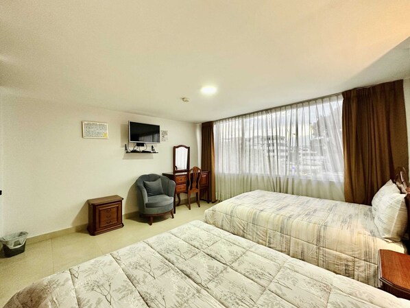Une chambre d’hôtel avec un lit, une chaise, un bureau, une télévision et une fenêtre avec des rideaux.