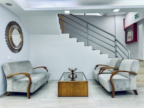 A modern lobby with a staircase, two armchairs, a glass coffee table, and a decorative mirror. - Hotel Tiwintza Internacional (Quito)