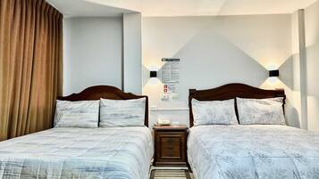 A double room with two beds, a nightstand, a wall-mounted light, and a bulletin board with information.