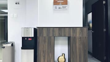 Een modern receptiebalie met een koffieapparaat, een prullenbak en een houten kastje met een vaas.