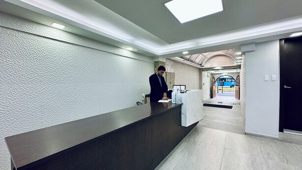 A reception desk with a modern design, a man working behind it, and a view of the entrance area with a blue car visible outside. - Hotel Tiwintza Internacional (Quito)