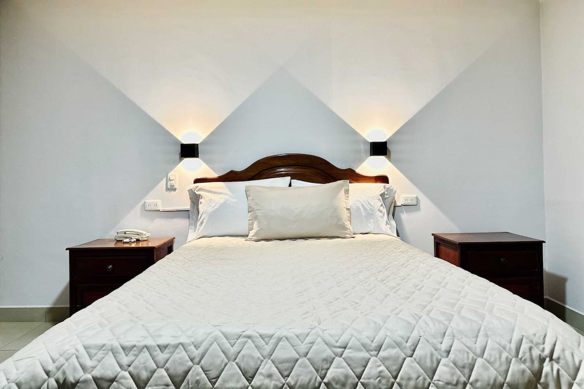A neatly made bed with a quilted cover, two bedside tables with lamps, and a wooden headboard.