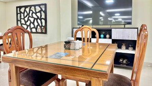 A dining area with a glass-top table, wooden chairs, a flat-screen TV, and decorative items on shelves. - Hotel Tiwintza Internacional (Quito)