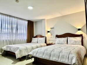 A hotel room with two single beds, a large window with sheer curtains, a wall-mounted night light, and a visible emergency exit sign. - Hotel Tiwintza Internacional (Quito)